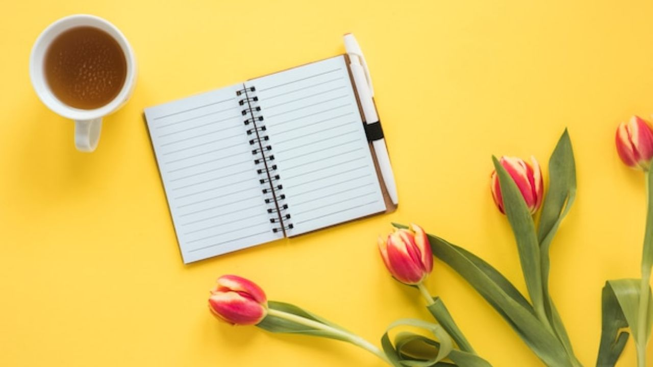 靠近一杯饮料和带绿叶的新鲜郁金香的笔记本